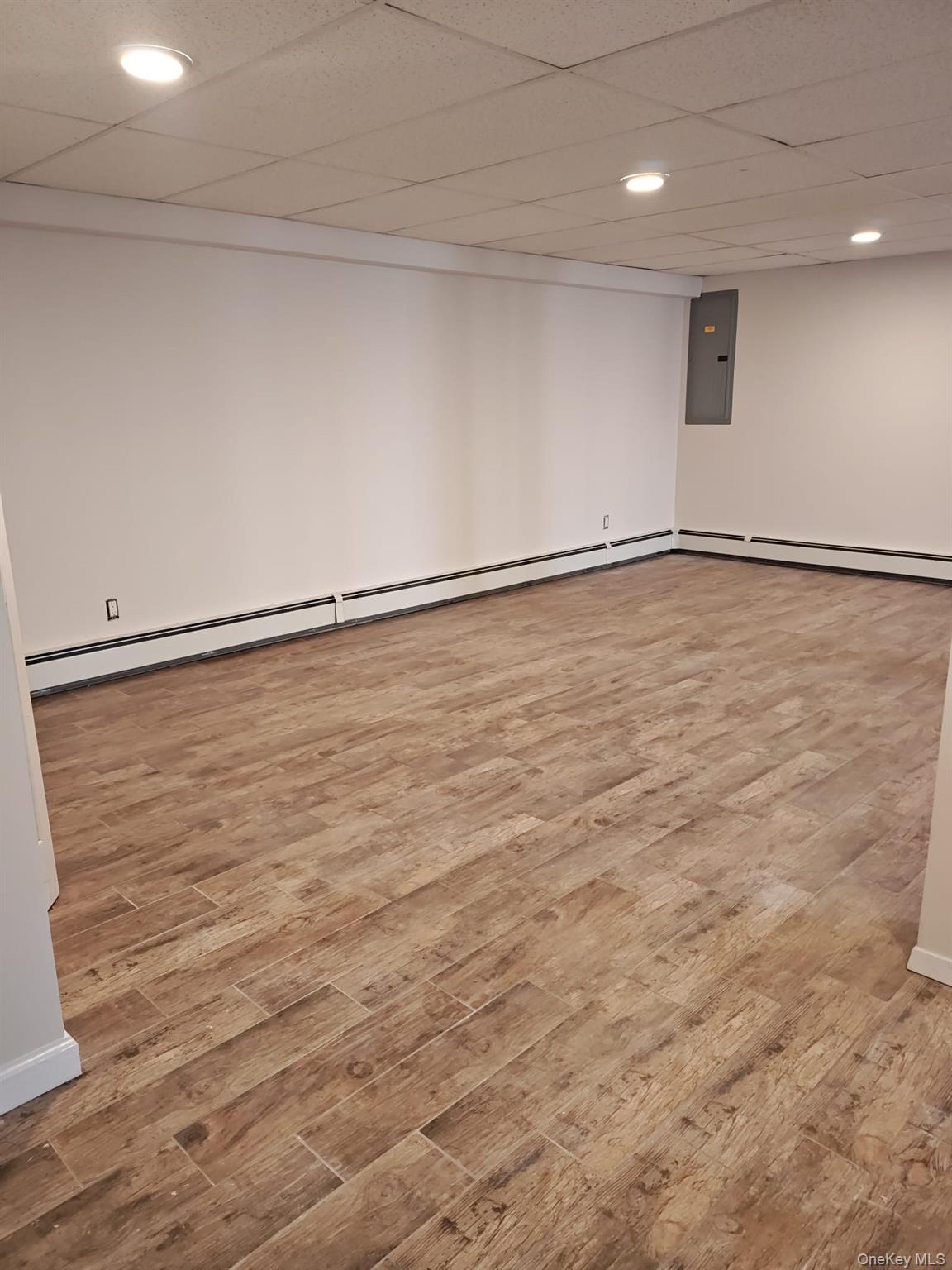 2354 North Wading River Road Wading River, NY 11792 - Photo 20 of 28 Finished below grade area featuring a drop ceiling, light wood-style floors, recessed lighting, electric panel, and a baseboard heating unit