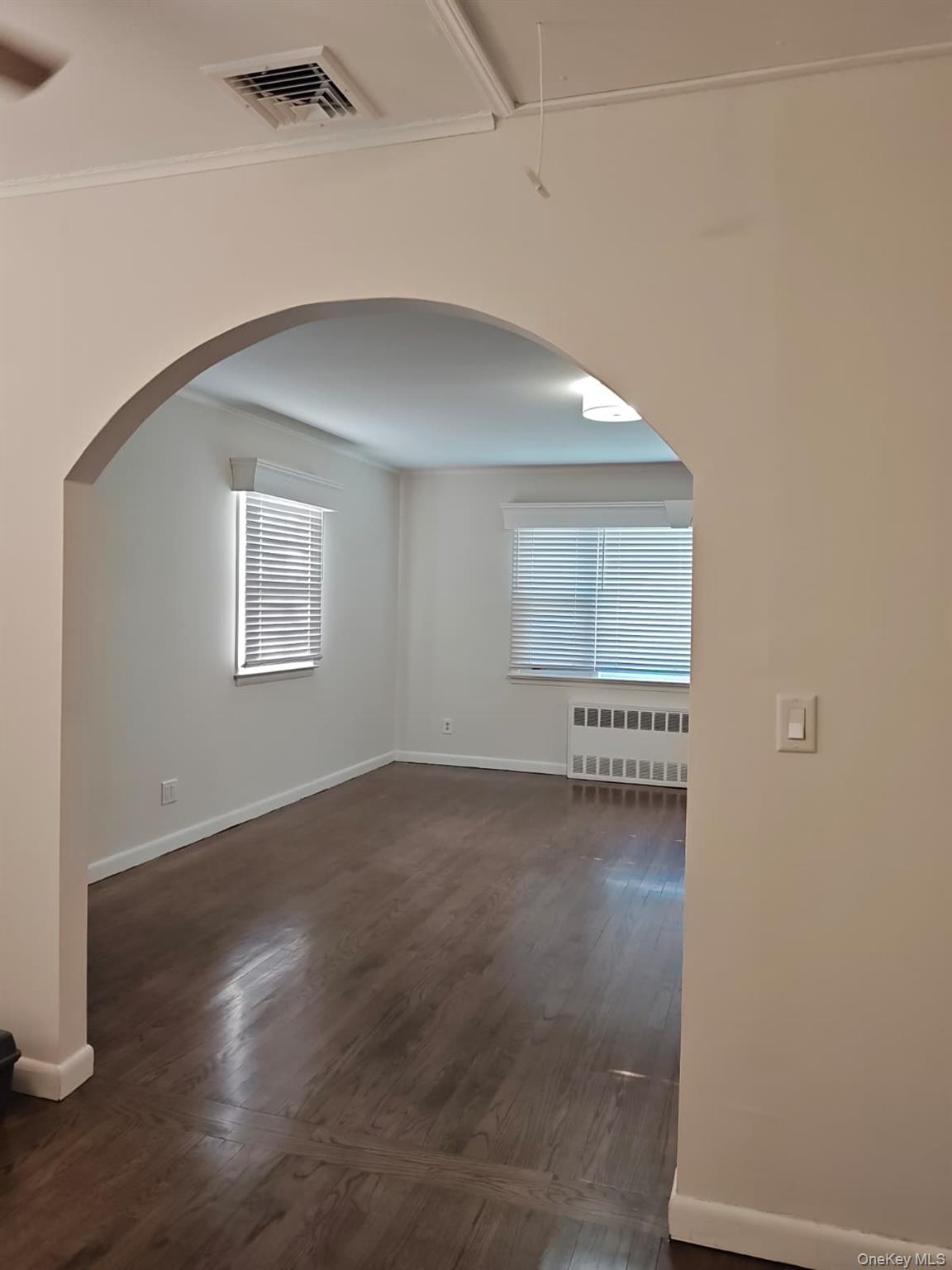 2354 North Wading River Road Wading River, NY 11792 - Photo 2 of 20 Empty room featuring arched walkways, radiator heating unit, dark wood-style floors, and attic access