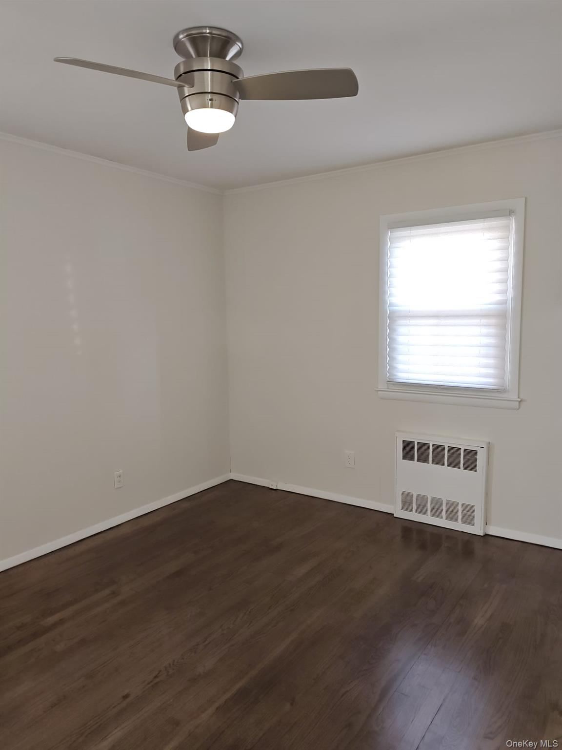 2354 North Wading River Road Wading River, NY 11792 - Photo 9 of 28 Empty room with ornamental molding, dark wood finished floors, radiator heating unit, and ceiling fan