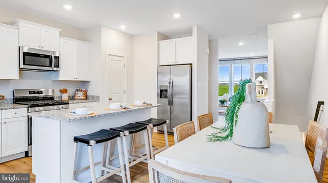 a kitchen with stainless steel appliances a sink a stove a refrigerator cabinets and a dining table with wooden floor