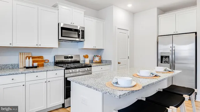 a kitchen with stainless steel appliances kitchen island granite countertop a sink a microwave a refrigerator and white cabinets