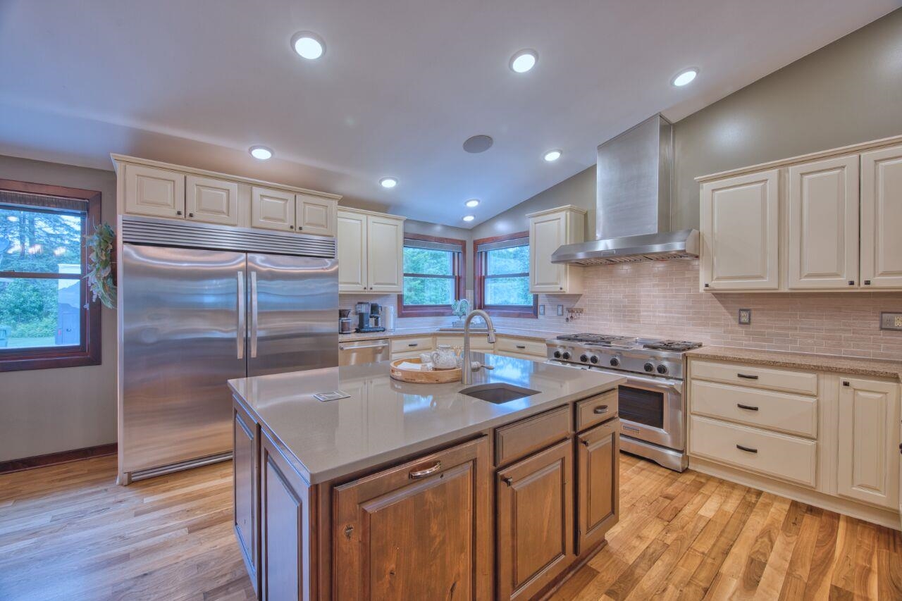 3557 Haverkamp Road Hibbing, MN 55746 - Photo 6 of 60 Kitchen with high end appliances, wall chimney exhaust hood, backsplash, light wood finished floors, and vaulted ceiling