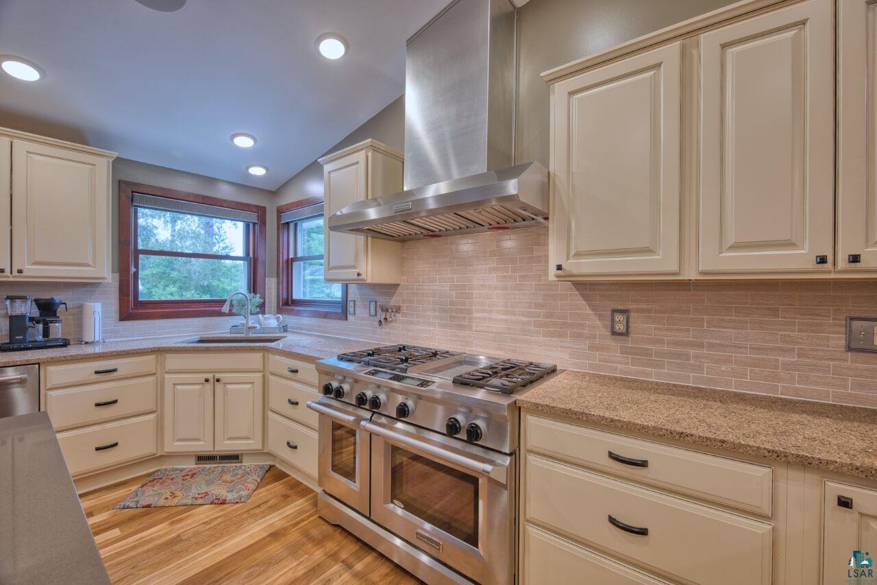 3557 Haverkamp Road Hibbing, MN 55746 - Photo 7 of 60 Kitchen featuring stainless steel appliances, wall chimney exhaust hood, light wood finished floors, tasteful backsplash, and lofted ceiling