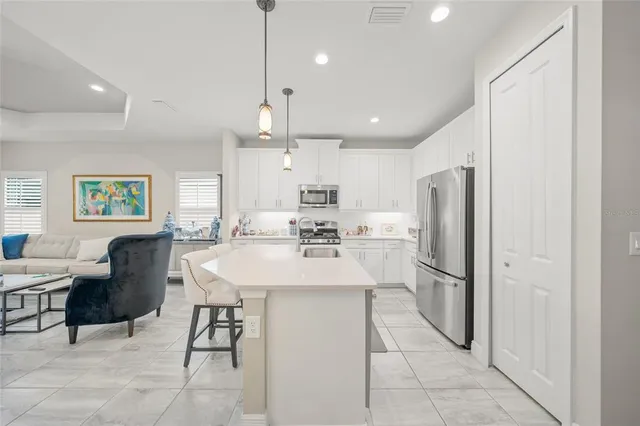 a kitchen with stainless steel appliances kitchen island granite countertop a refrigerator a sink a stove and white cabinets with wooden floor