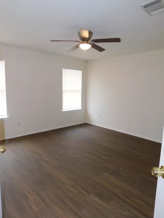 an empty room with wooden floor fan and windows
