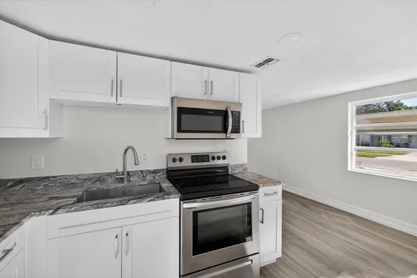 a kitchen with granite countertop a stove a microwave a sink and cabinets