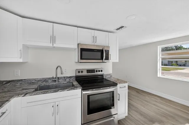 a kitchen with granite countertop a stove a microwave a sink and cabinets