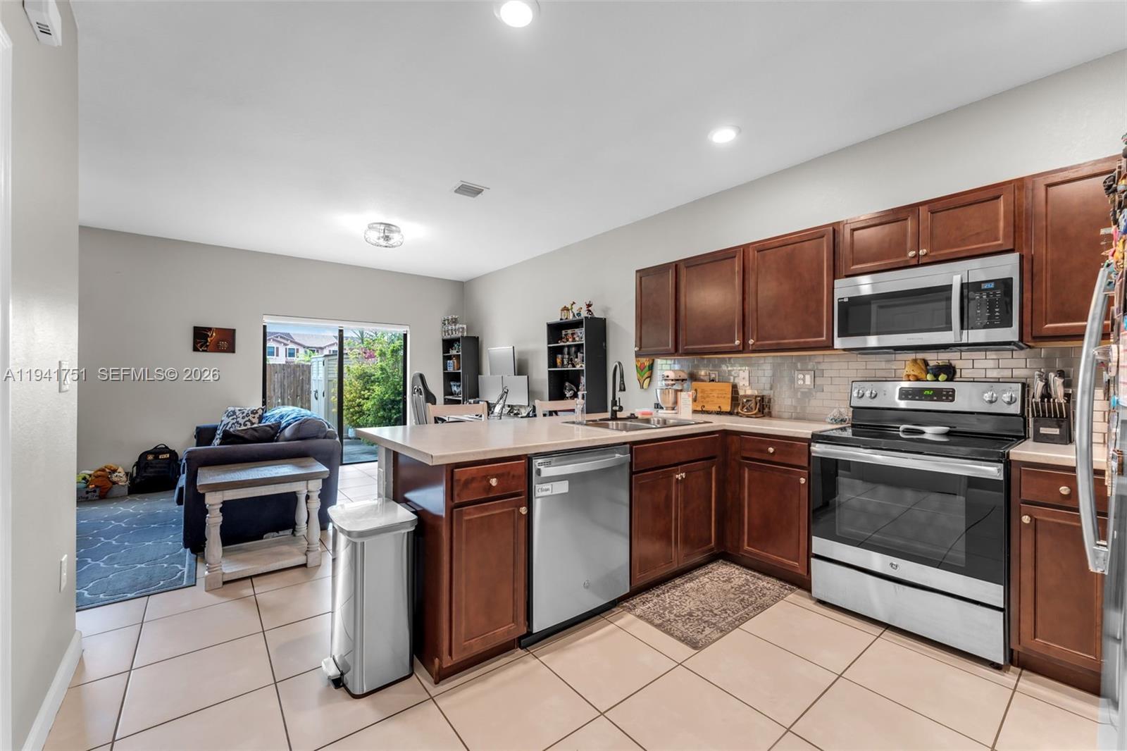 3763 Southeast 2nd Street Homestead, FL 33033 - Photo 7 of 48 a kitchen with stainless steel appliances granite countertop a stove top oven a sink dishwasher a dining table and chairs with wooden cabinets