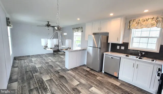 a kitchen with stainless steel appliances granite countertop a refrigerator a sink dishwasher a stove and white countertops with wooden floor