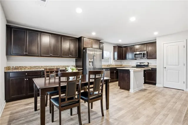 a kitchen with stainless steel appliances granite countertop a stove a refrigerator a kitchen island a dining table and chairs with wooden floor