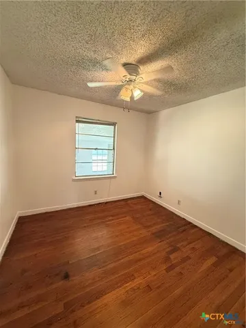 an empty room with wooden floor chandelier fan and windows