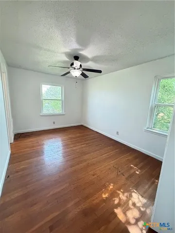 an empty room with wooden floor chandelier fan and windows