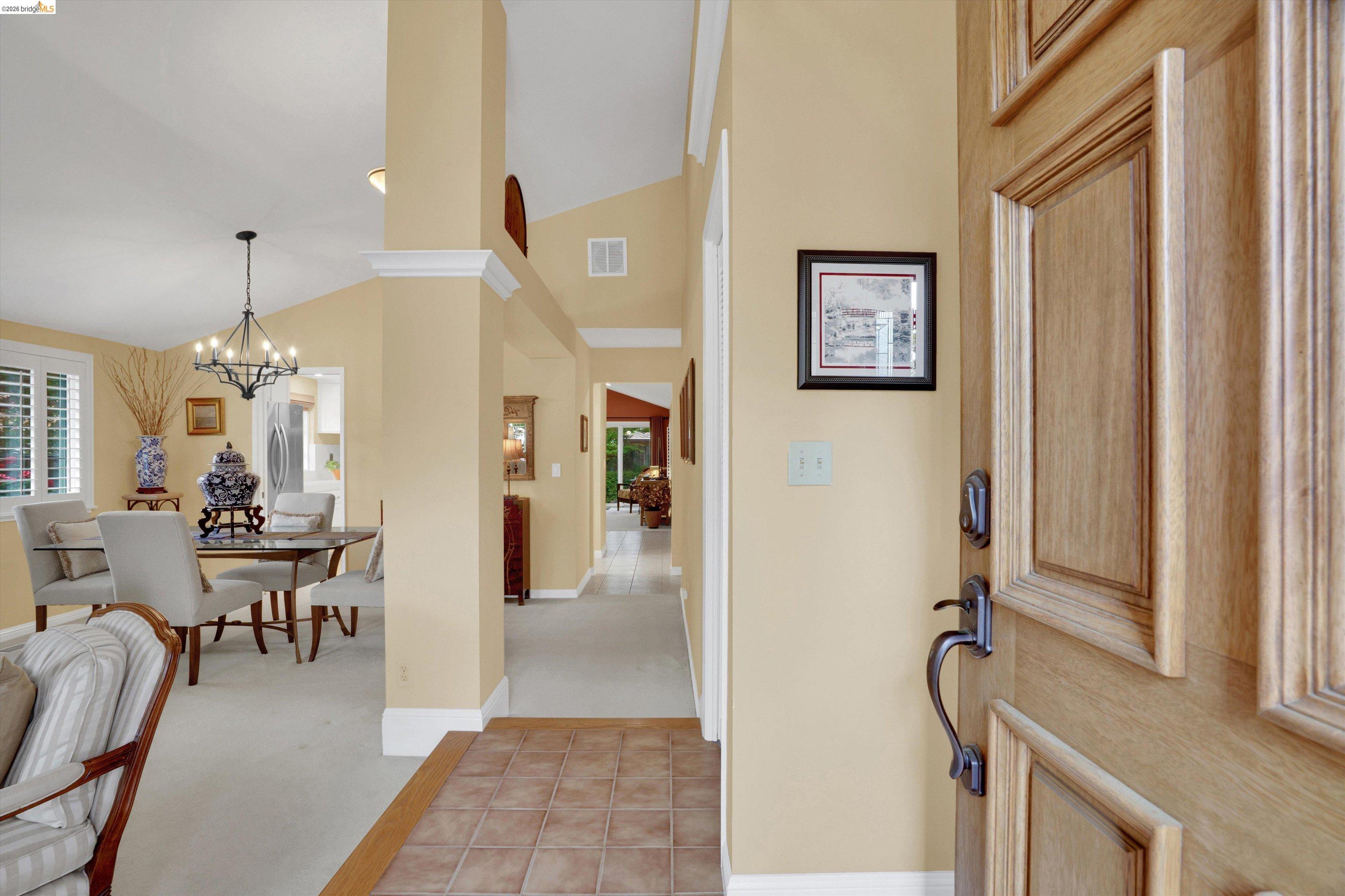 5001 St Garrett Court Concord, CA 94521 - Photo 11 of 45 Entryway featuring a paneled wood-finish door with dark hardware, leading to an interior with vaulted ceilings, crown molding, and a chandelier-lit dining area