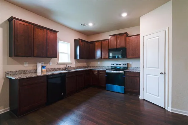 a kitchen with stainless steel appliances granite countertop wooden cabinets a stove a sink and a wooden floor