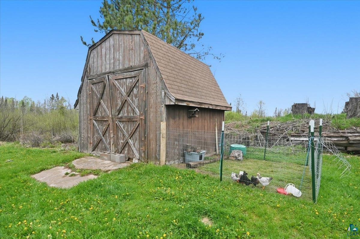 5190 County Road M Gordon, WI 54838 - Photo 23 of 31 Wood-sided barn structure featuring double entry doors with cross-brace detailing, a shingled roof, and a small birdhouse attachment