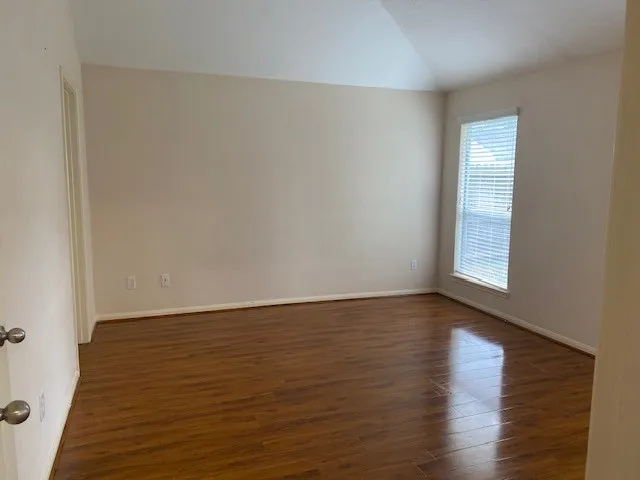 a view of an empty room with wooden floor and a window