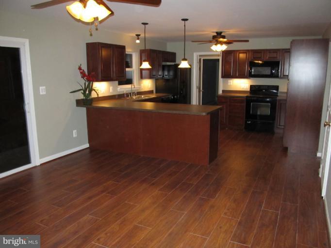 11635 Bald Bluff Road Lusby, MD 20657 - Photo 8 of 19 a kitchen with stainless steel appliances kitchen island granite countertop a stove a refrigerator a sink a dining table and chairs with wooden floor
