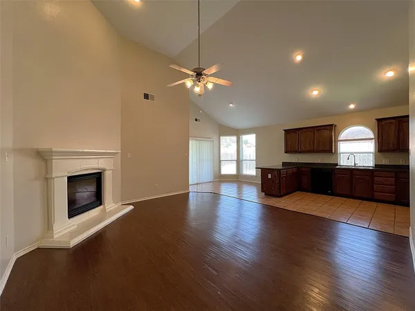 a view of an empty room with wooden floor and a kitchen