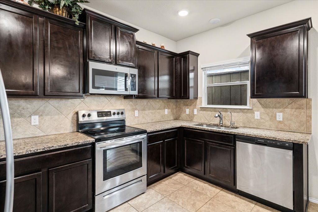 212 Plata Lane Jarrell, TX 76537 - Photo 12 of 30 Kitchen with stainless steel appliances, dark wood finish cabinets, light stone counters, backsplash, and light tile patterned floors