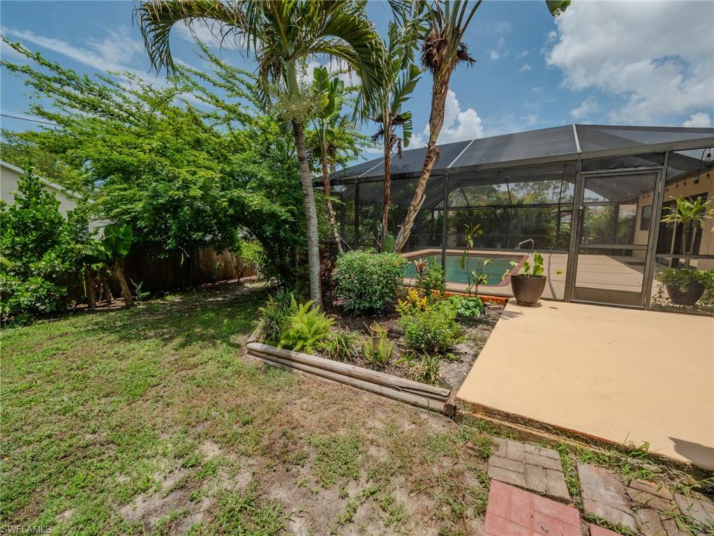 18414 Tulip Road Fort Myers, FL 33967 - Photo 35 of 37 Screened outdoor swimming pool enclosure with a surrounding deck, complemented by a landscaped garden bed featuring palm trees and diverse plantings