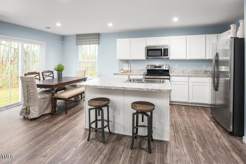 237 Suburban Meadow Pass Wendell, NC 27591 - Photo 5 of 15 a kitchen with stainless steel appliances granite countertop wooden floors a stove a microwave a center island and a window