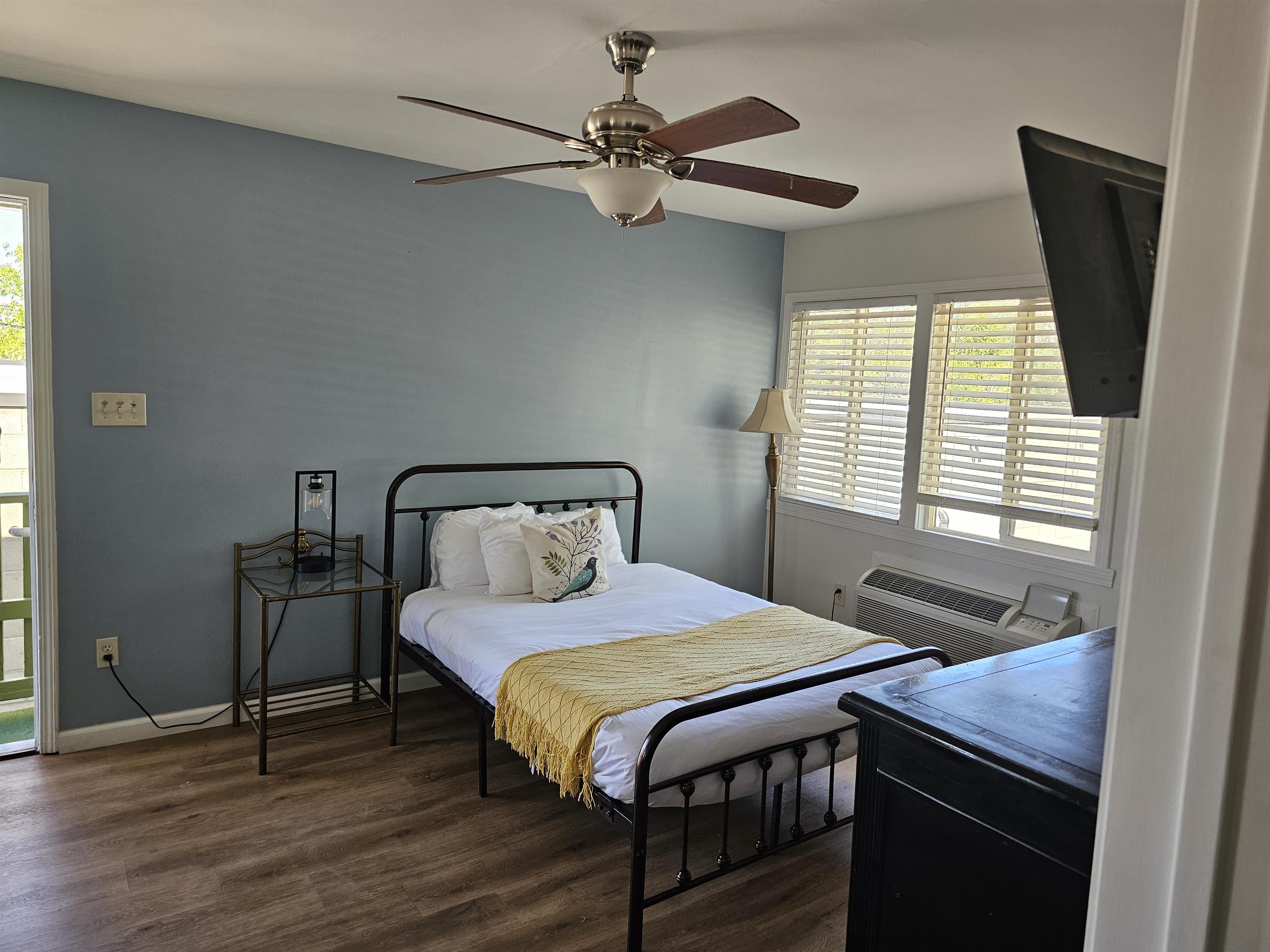 461 High Street Bishop, CA 93514 - Photo 7 of 10 Interior space featuring wood-finish flooring, a ceiling fan with light fixture, light blue wall accent, multiple windows with blinds, and a window-mounted air conditioning unit