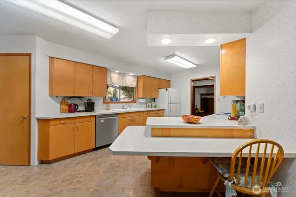 a kitchen with stainless steel appliances kitchen island granite countertop a refrigerator a stove top oven a sink dishwasher and white cabinets next to a window