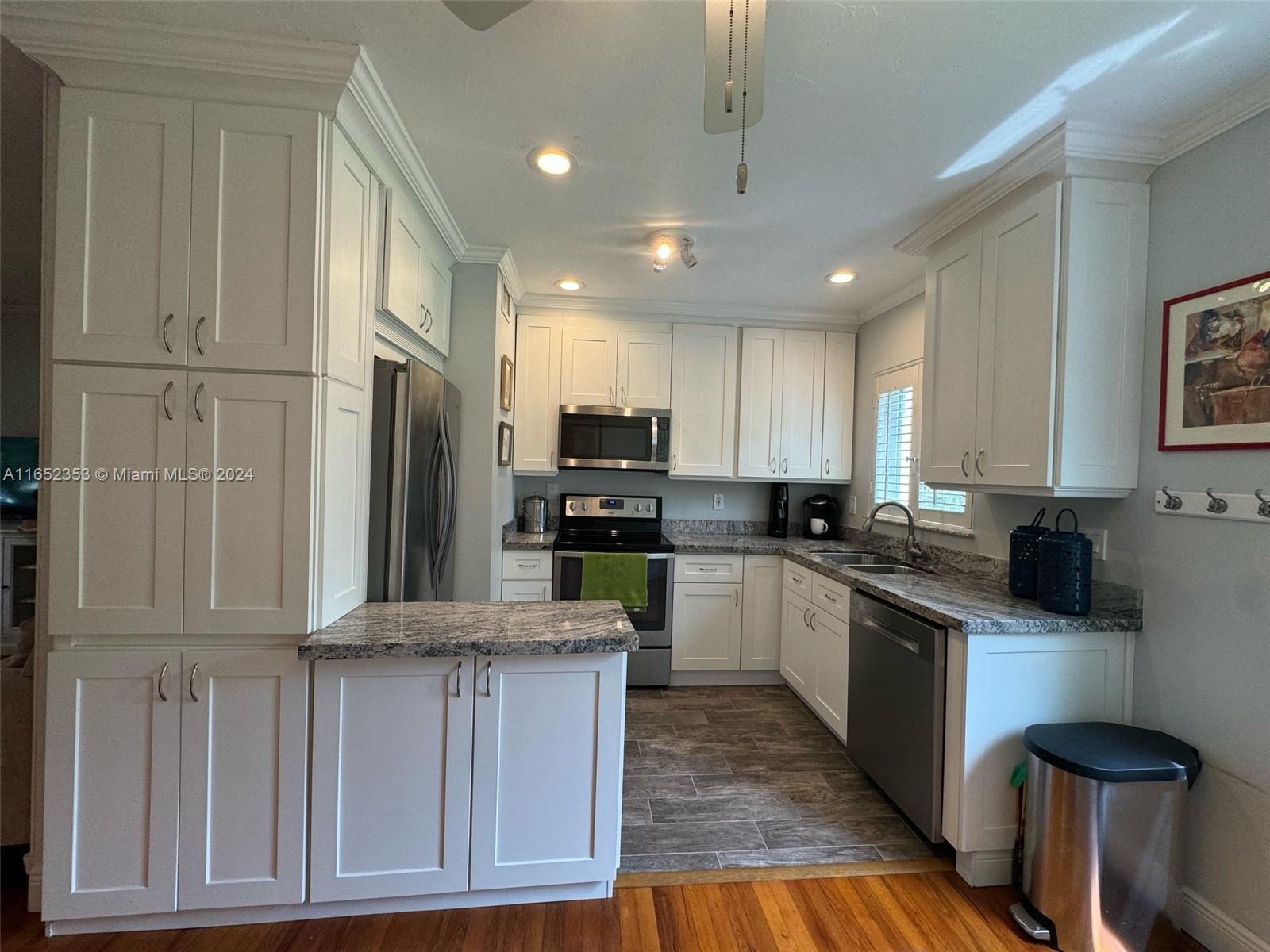 5530 Southwest 76th Street, Unit A Miami, FL 33143 - Photo 1 of 10 a kitchen with kitchen island granite countertop a refrigerator oven a sink dishwasher and white cabinets with wooden floor