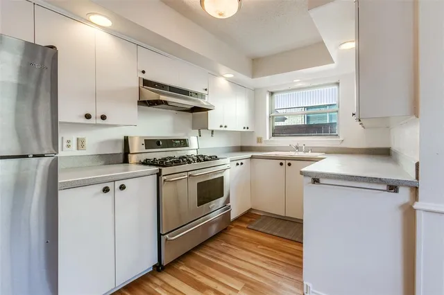 a white kitchen with stainless steel appliances granite countertop a stove a sink and a refrigerator