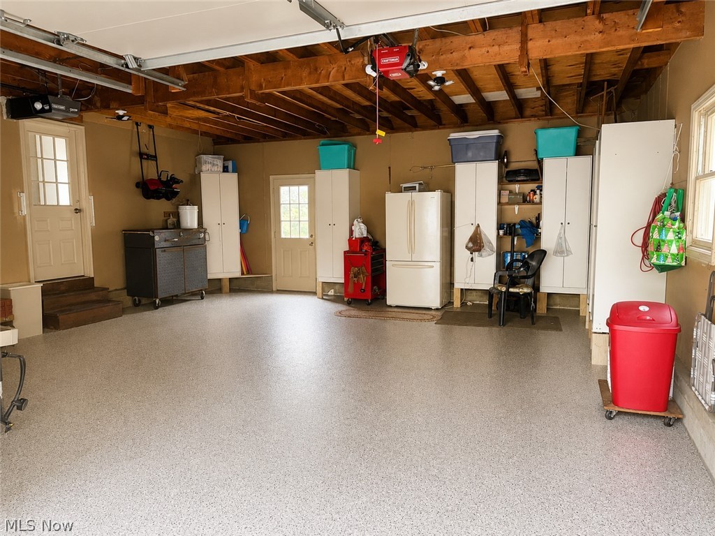 6155 Gibson Road Canfield, OH 44406 - Photo 38 of 43 Spacious garage featuring a light-toned epoxy floor finish, exposed wood ceiling beams, multiple built-in storage cabinets, and two distinct entry doors