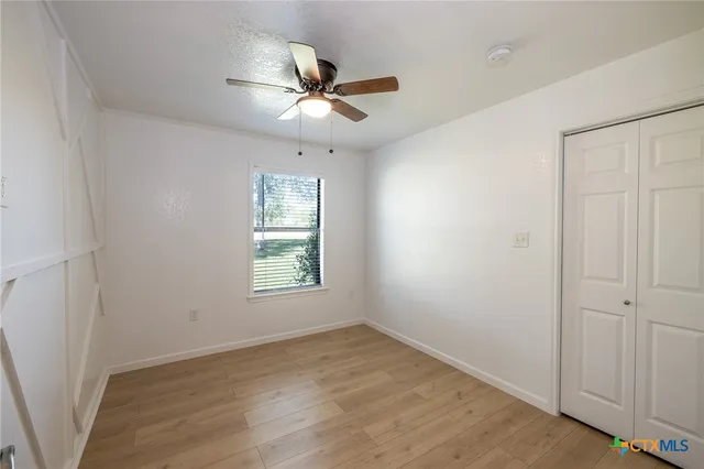 an empty room with wooden floor fan and windows
