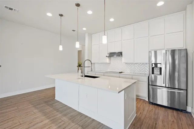 a kitchen with stainless steel appliances granite countertop a sink a oven a refrigerator and white cabinets with wooden floor