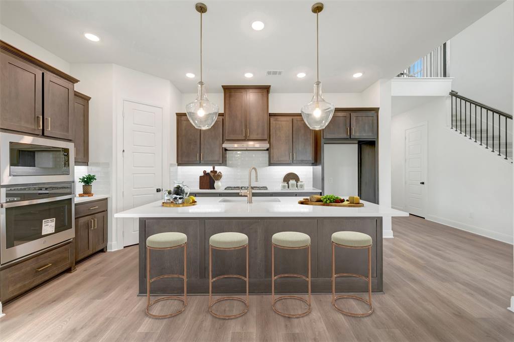 1908 Cola Drive Van Alstyne, TX 75495 - Photo 16 of 29 Kitchen featuring an expansive island with a white countertop, recessed lighting, wood-finish flooring, dark wood cabinetry, and stainless steel appliances