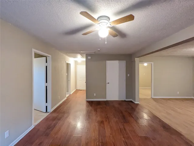 a view of an empty room with wooden floor and a ceiling fan