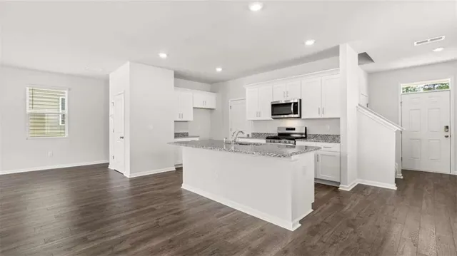 a kitchen with stainless steel appliances granite countertop a stove top oven a sink a refrigerator white cabinets and wooden floor