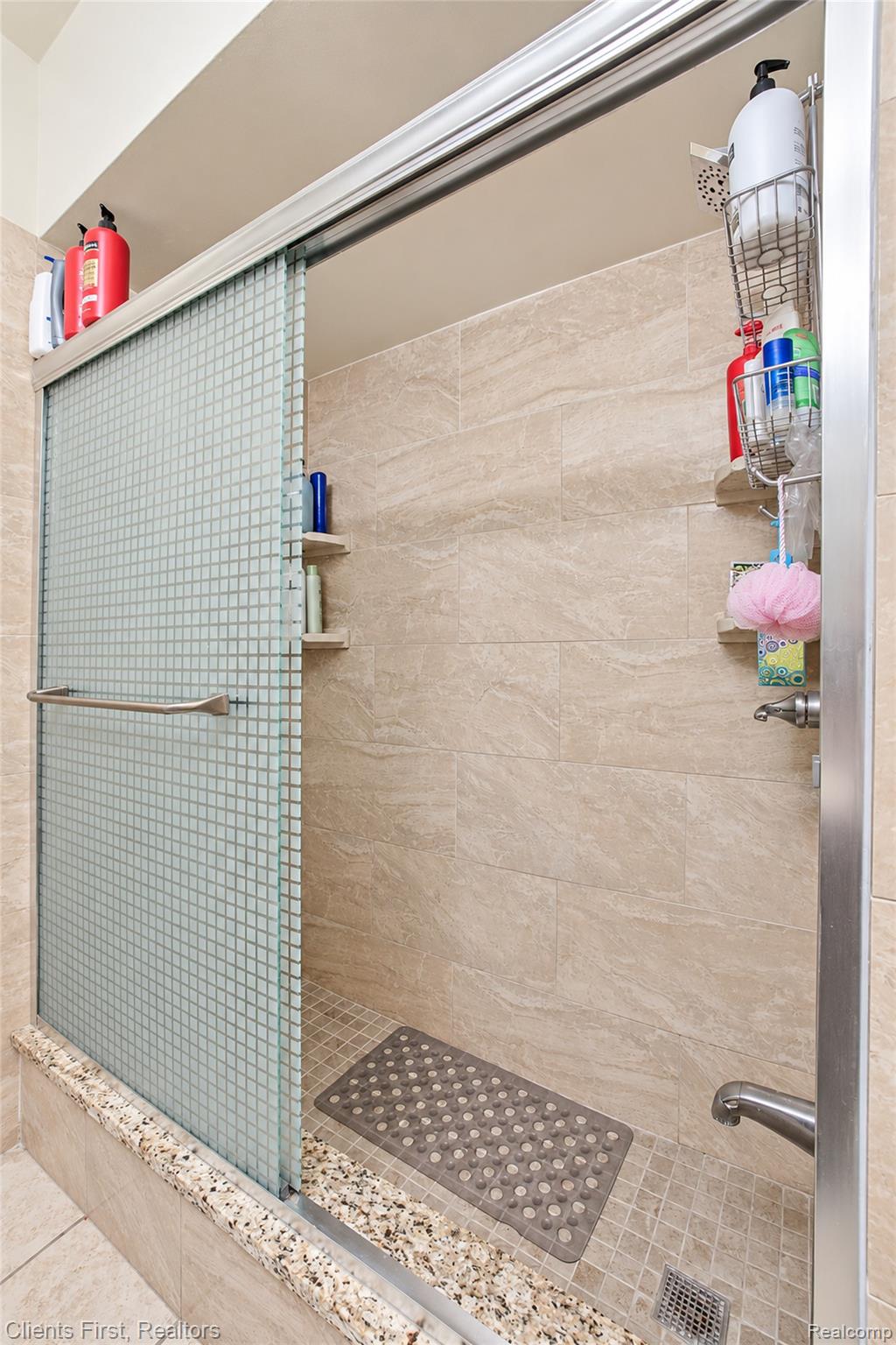 5430 Chase Road Dearborn, MI 48126 - Photo 11 of 34 Sliding shower door with textured glass panel, tiled shower walls, built-in corner shelving, and mosaic tile shower floor