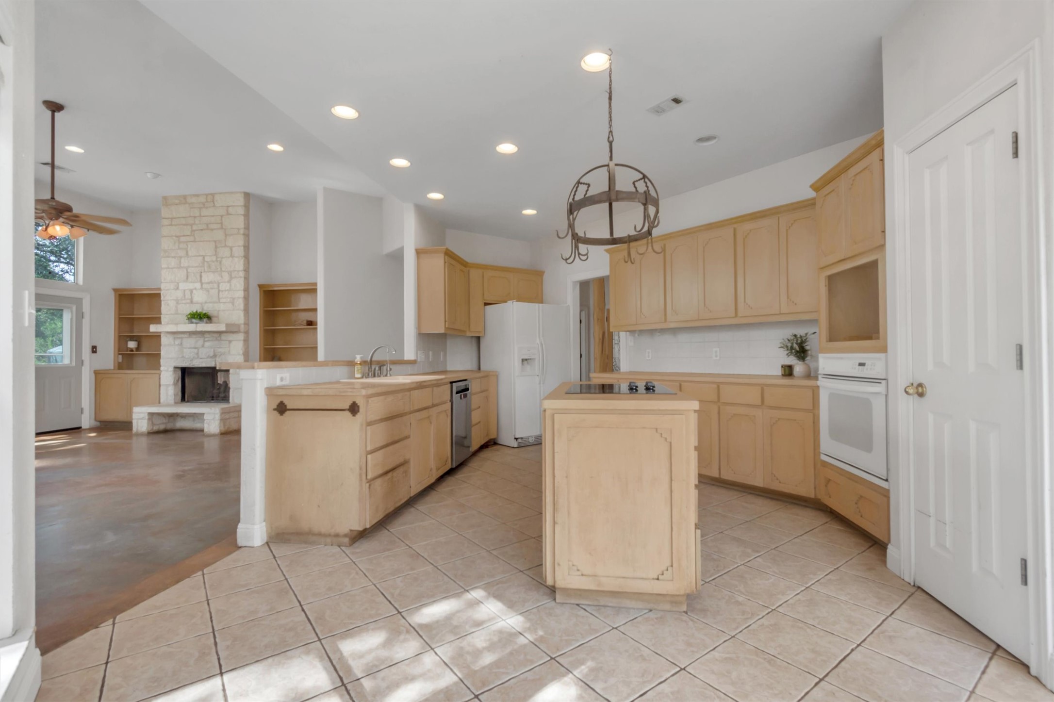1120 Meadow Ridge Drive Austin, TX 78737 - Photo 12 of 40 A spacious kitchen with light-toned cabinetry and tile flooring opens to a living area featuring a stone fireplace.