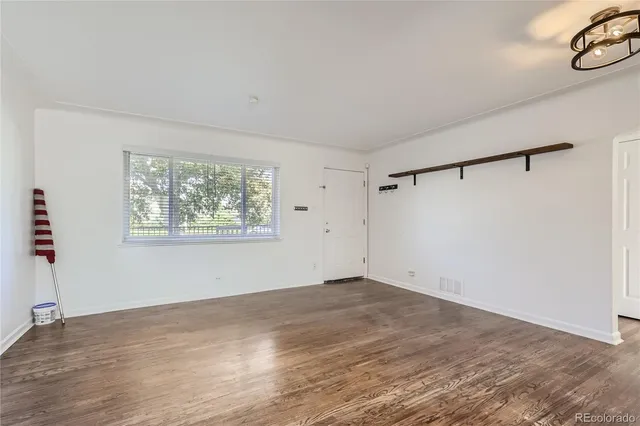 a view of an empty room with a window and hardwood floor