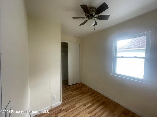 a view of empty room with wooden floor and fan