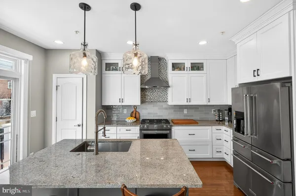 a kitchen with stainless steel appliances granite countertop a refrigerator a sink dishwasher and white cabinets with wooden floor