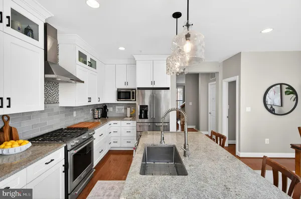 a kitchen with stainless steel appliances kitchen island granite countertop a refrigerator a stove a sink dishwasher and white cabinets with wooden floor