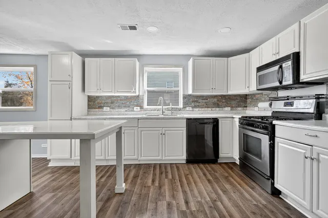 a kitchen with stainless steel appliances granite countertop a stove top oven a sink dishwasher and white cabinets with wooden floor