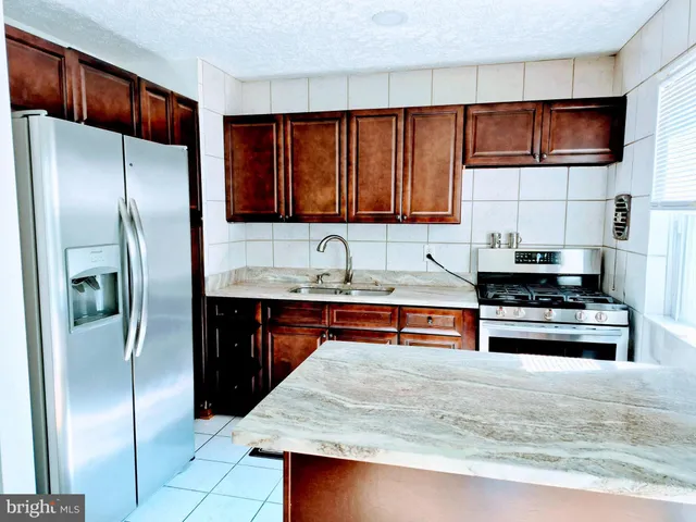 a kitchen with stainless steel appliances granite countertop a refrigerator a stove and a sink with wooden cabinets