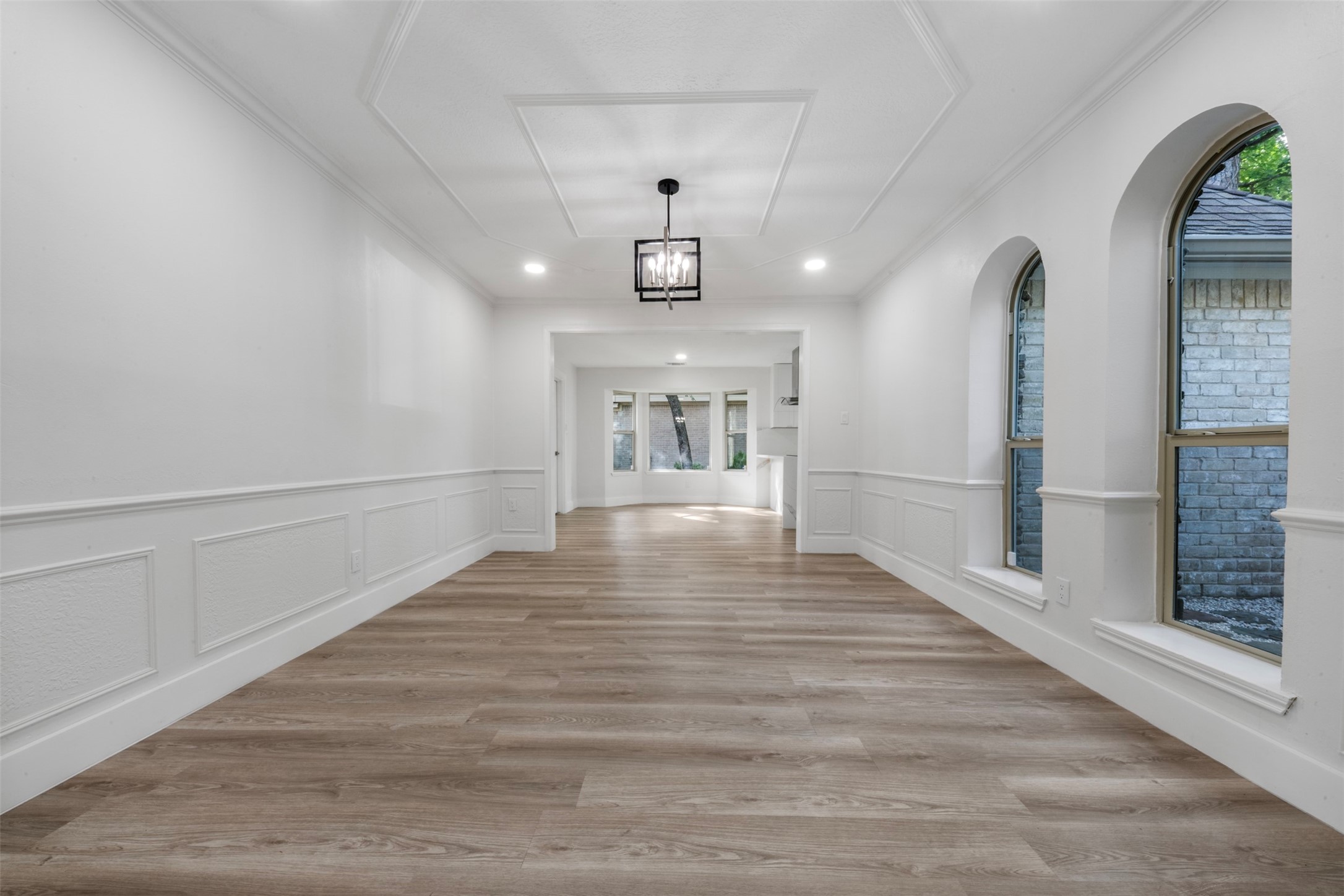 9543 Enstone Circle Spring, TX 77379 - Photo 14 of 50 This photo showcases a spacious, light-filled dining room with elegant wainscoting and wood flooring. It features a modern ceiling light fixture and large arched windows, creating an inviting atmosphere. The space opens to an adjacent room, enhancing the flow of the home.