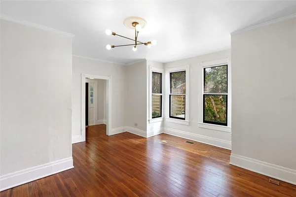 an empty room with wooden floor chandelier and windows