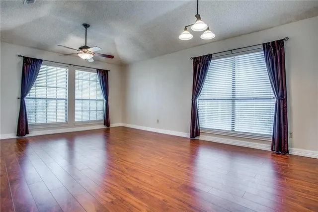 an empty room with wooden floor chandelier and windows