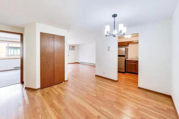 a view of empty room with wooden floor and kitchen