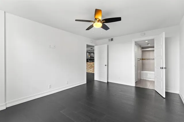 a view of an empty room with wooden floor and a ceiling fan