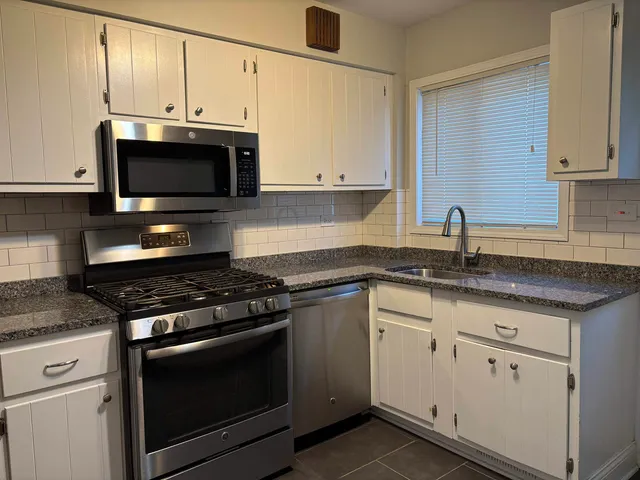 a kitchen with granite countertop a sink dishwasher a stove and a microwave oven with cabinets