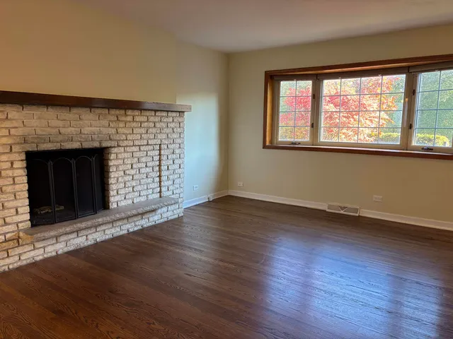 an empty room with wooden floor fireplace and windows
